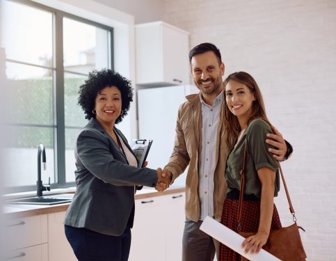 Happy real estate agent handshaking with a couple of buyers and looking at camera. Copy space.