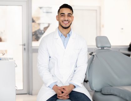 Stomatological Services. Handsome Arab Male Dentist Posing At Workplace In Clinic Interior, Middle Eastern Stomatologist Doctor In Uniform Looking And Smiling At Camera, Ready For Check Up